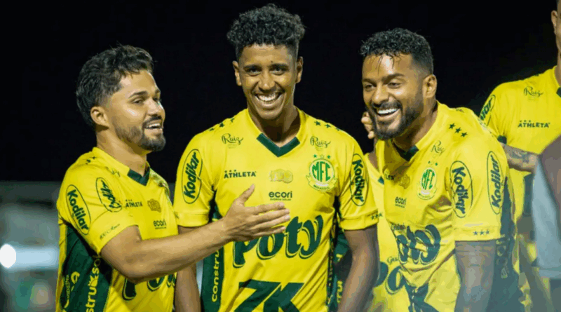 Três jogadores do Mirassol, usando uniforme amarelo com detalhes verdes, comemoram sorrindo em campo durante a noite. O atleta ao centro aparece rindo, enquanto os dois ao lado gesticulam e celebram ao seu redor.