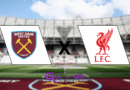 Imagem com fundo desfocado do estádio do West Ham, mostrando o gramado e as arquibancadas. Ao centro, há um grande “X” preto separando dois escudos: à esquerda, o escudo do West Ham United em bordô com duas marretas cruzadas em amarelo; à direita, o escudo do Liverpool em vermelho com o Liver Bird. Na parte inferior, o logo roxo do portal “Gol a Gol”.