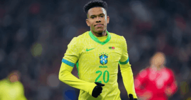 Jogador da seleção brasileira com a camisa amarela número 20 corre em campo durante a partida, usando luvas pretas e expressão concentrada; o fundo mostra o estádio desfocado.