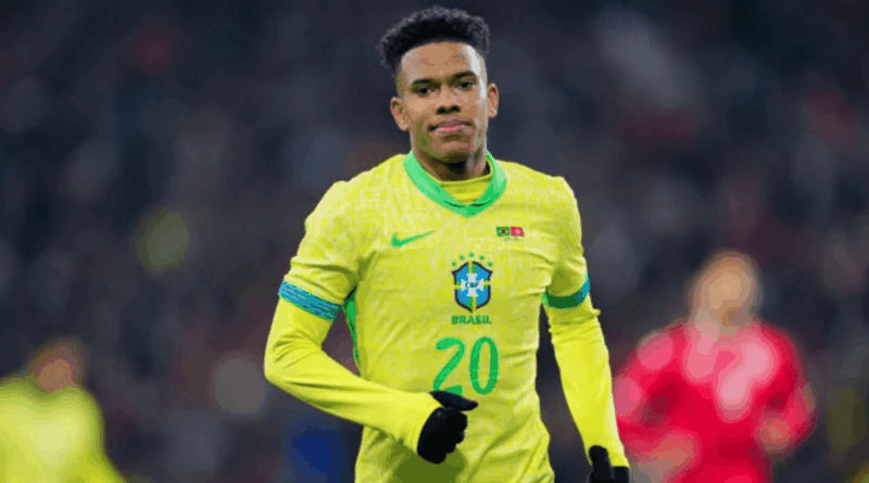 Jogador da seleção brasileira com a camisa amarela número 20 corre em campo durante a partida, usando luvas pretas e expressão concentrada; o fundo mostra o estádio desfocado.