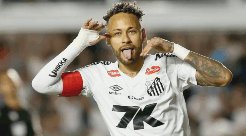 Jogador do Santos comemora gol fazendo gesto com as mãos ao lado do rosto e mostrando a língua; ele veste uniforme branco com braçadeira vermelha e aparece em primeiro plano, com o estádio desfocado ao fundo.