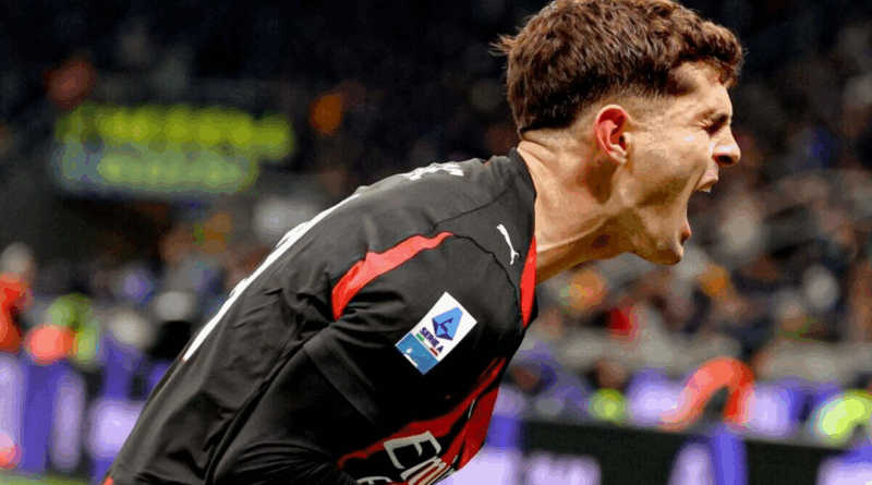 Jogador do Milan, vestindo uniforme preto com detalhes vermelhos, comemora gritando com intensidade, inclinado para frente, com as veias do pescoço saltadas. O fundo mostra arquibancadas desfocadas e luzes do estádio.